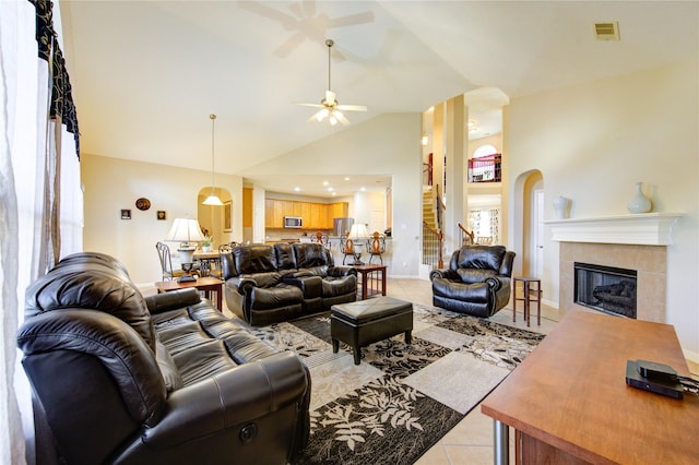 living area with light tile patterned floors, high vaulted ceiling, ceiling fan, a tile fireplace, and visible vents