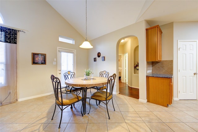 dining space with high vaulted ceiling, arched walkways, light tile patterned flooring, and baseboards