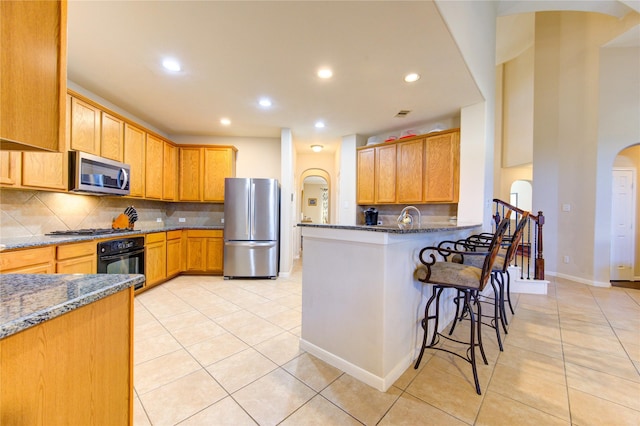 kitchen featuring appliances with stainless steel finishes, a kitchen breakfast bar, decorative backsplash, and dark stone countertops