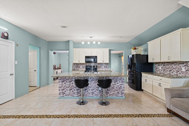 kitchen featuring light tile patterned floors, a breakfast bar area, stone counters, black appliances, and a center island with sink