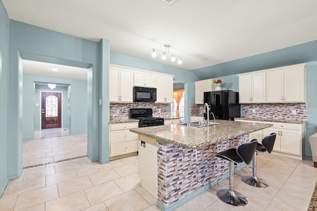 kitchen featuring an island with sink, sink, a kitchen breakfast bar, light stone counters, and black appliances
