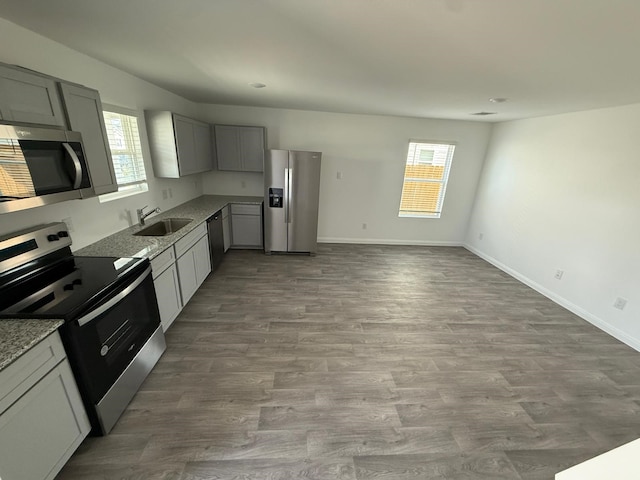 kitchen with sink, gray cabinets, hardwood / wood-style floors, stainless steel appliances, and light stone counters