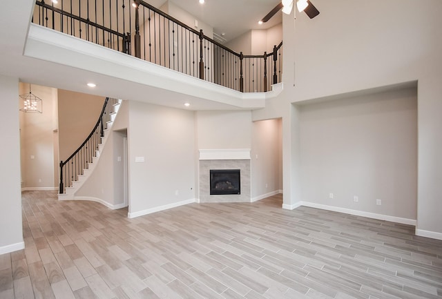 unfurnished living room featuring a tile fireplace, a towering ceiling, ceiling fan with notable chandelier, and light hardwood / wood-style floors