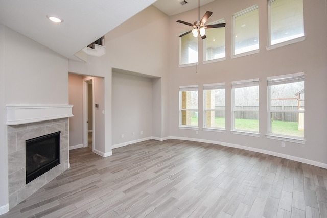 unfurnished living room with ceiling fan, plenty of natural light, a tiled fireplace, and light hardwood / wood-style flooring