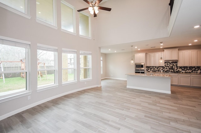 kitchen with tasteful backsplash, light stone counters, hanging light fixtures, a center island with sink, and stainless steel appliances