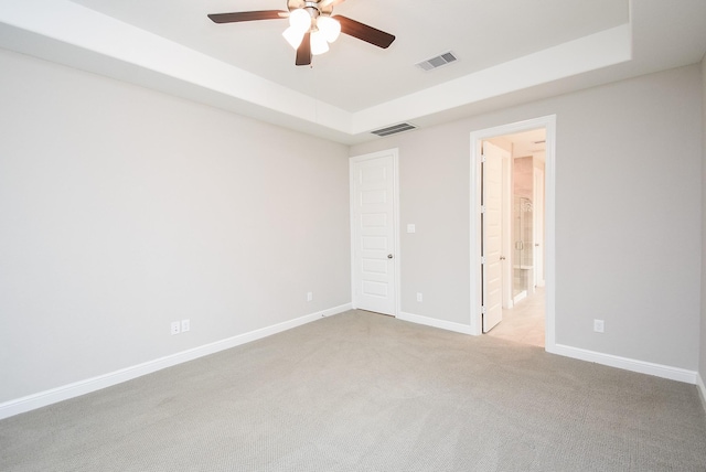 interior space with ceiling fan, ensuite bath, a raised ceiling, and light carpet