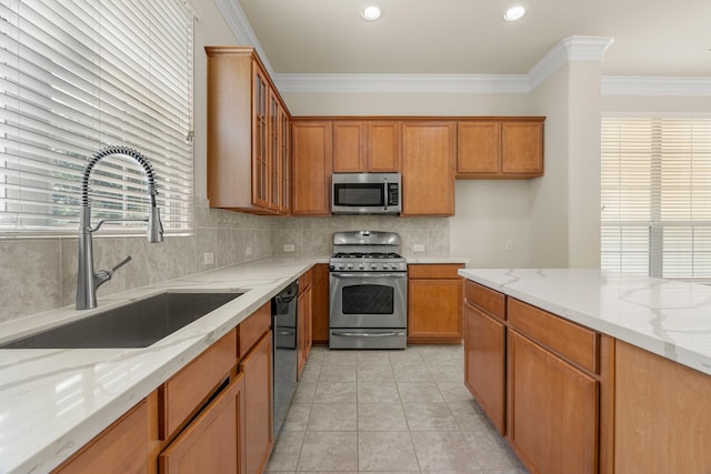 kitchen featuring stainless steel appliances, a sink, light stone countertops, brown cabinetry, and crown molding