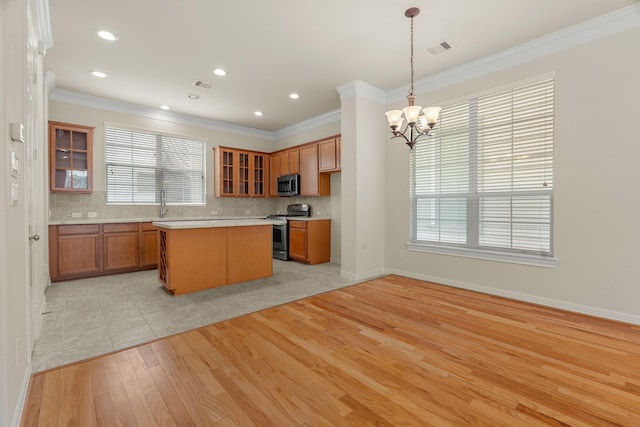 kitchen featuring pendant lighting, brown cabinets, light countertops, appliances with stainless steel finishes, and glass insert cabinets