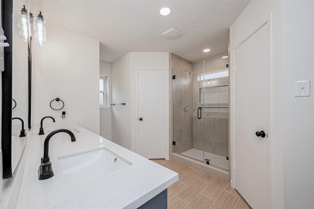 bathroom with a shower with door, vanity, and a textured ceiling