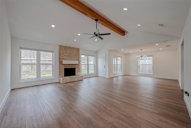 unfurnished living room featuring ceiling fan with notable chandelier, a fireplace, hardwood / wood-style floors, and vaulted ceiling with beams