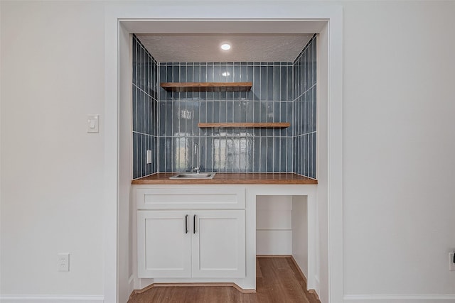 bar with sink, a textured ceiling, white cabinets, and hardwood / wood-style flooring