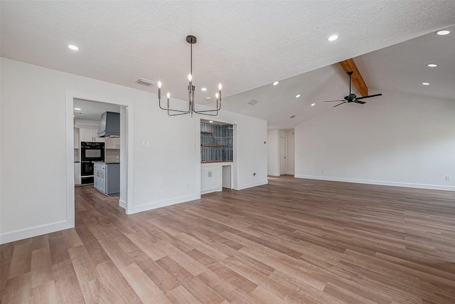 unfurnished living room featuring ceiling fan with notable chandelier, light hardwood / wood-style flooring, lofted ceiling with beams, and a textured ceiling