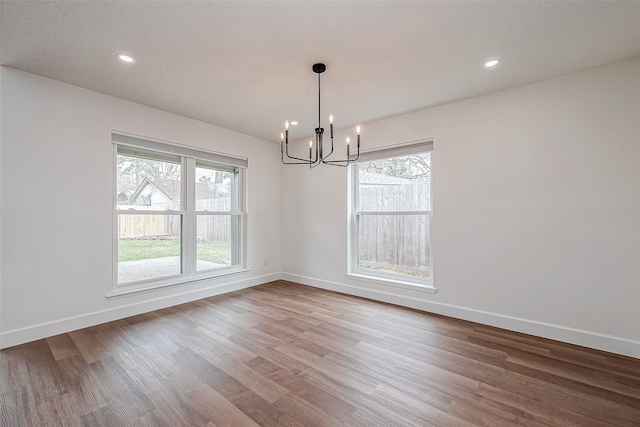 unfurnished dining area featuring an inviting chandelier, hardwood / wood-style floors, a textured ceiling, and a wealth of natural light