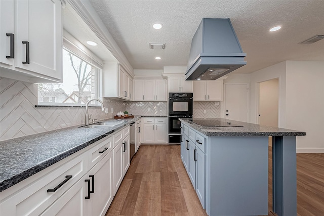 kitchen featuring sink, white cabinets, black appliances, custom range hood, and light hardwood / wood-style flooring