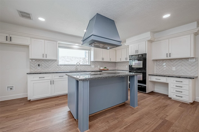 kitchen with custom exhaust hood, a center island, white cabinets, light hardwood / wood-style floors, and black appliances