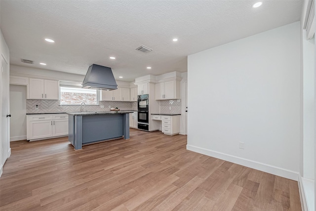 kitchen featuring custom range hood, a kitchen island, black double oven, light hardwood / wood-style floors, and white cabinets