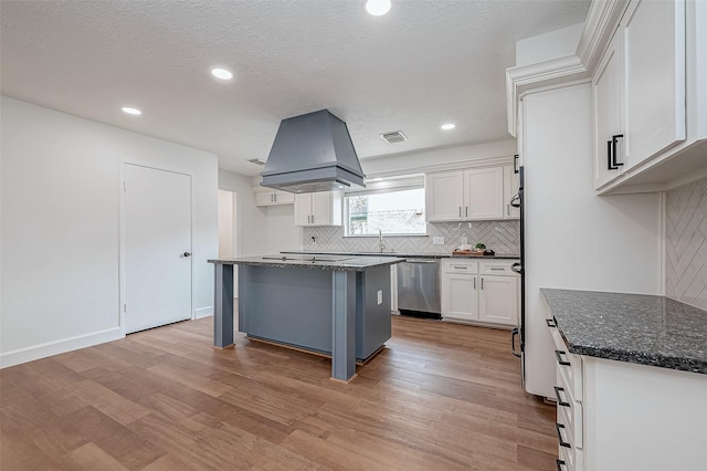 kitchen featuring white cabinetry, dark stone countertops, custom range hood, a kitchen island, and stainless steel dishwasher