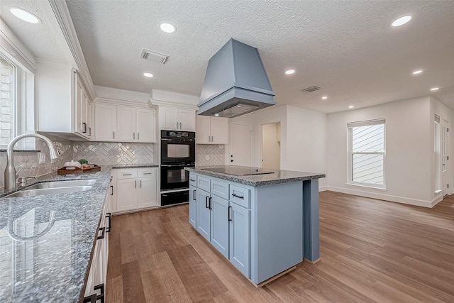 kitchen featuring sink, island range hood, a kitchen island, white cabinets, and black appliances