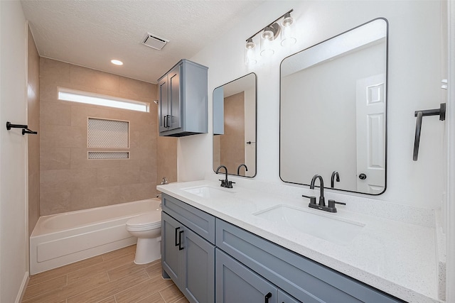 full bathroom featuring tiled shower / bath combo, vanity, hardwood / wood-style flooring, toilet, and a textured ceiling