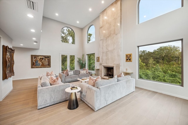 living room featuring a healthy amount of sunlight, a fireplace, light hardwood / wood-style floors, and a towering ceiling