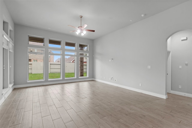 spare room with arched walkways, baseboards, ceiling fan, and light wood finished floors