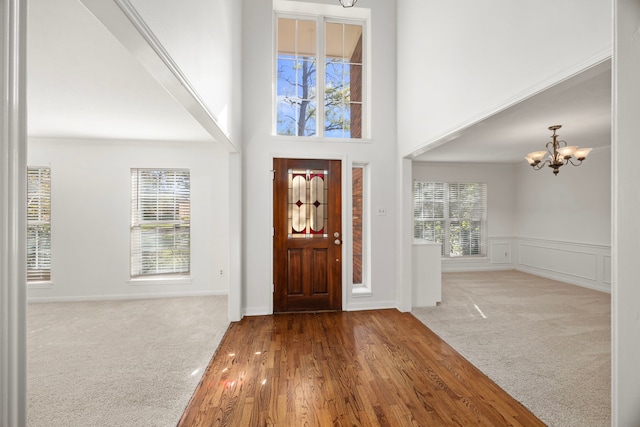carpeted entrance foyer featuring an inviting chandelier, a wainscoted wall, wood finished floors, and a high ceiling
