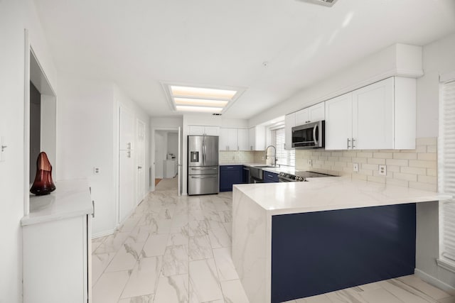 kitchen with appliances with stainless steel finishes, tasteful backsplash, white cabinetry, sink, and kitchen peninsula