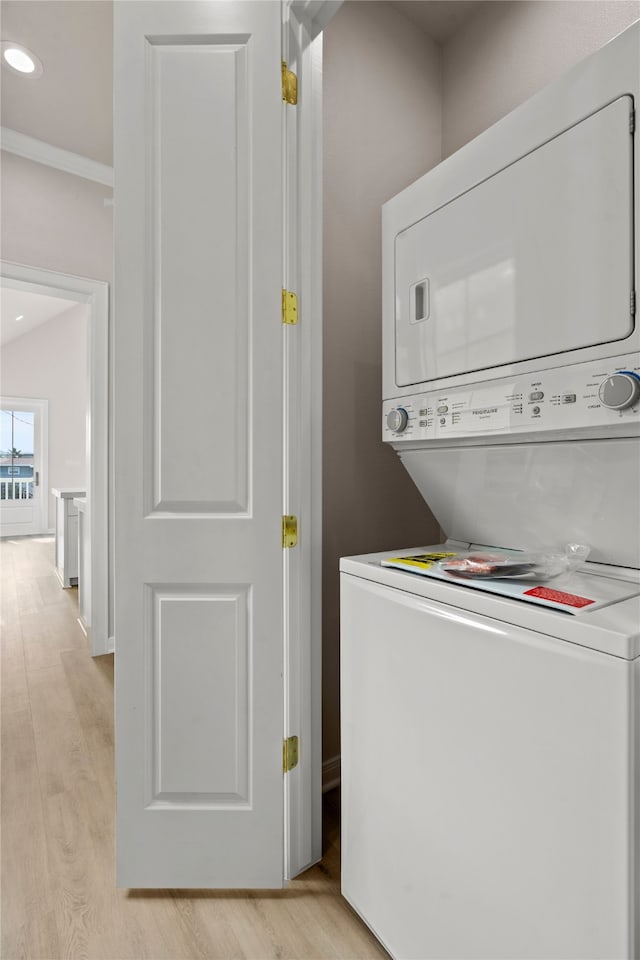 laundry room featuring stacked washing maching and dryer, crown molding, and light hardwood / wood-style flooring