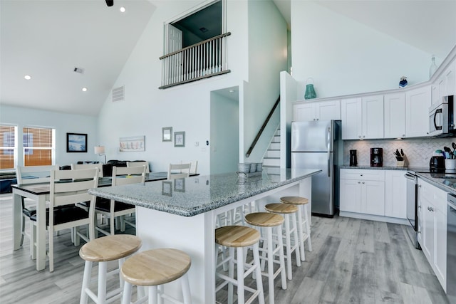 kitchen featuring appliances with stainless steel finishes, dark stone countertops, white cabinets, a kitchen bar, and a center island