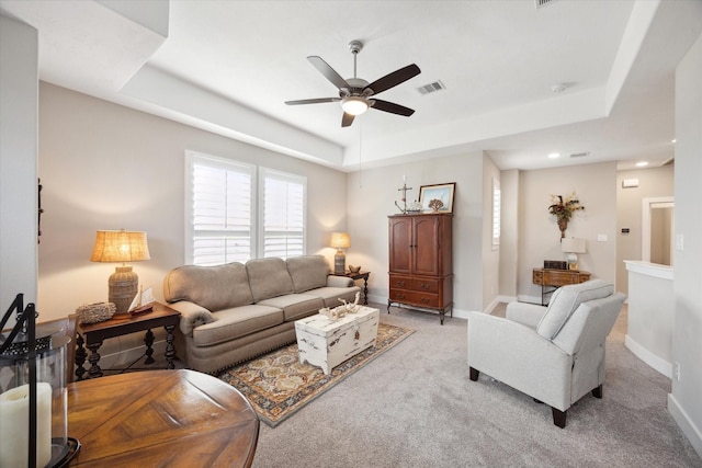 living room featuring a raised ceiling, light carpet, and ceiling fan