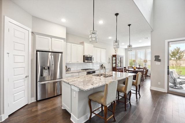 kitchen featuring hanging light fixtures, stainless steel appliances, an island with sink, and white cabinets