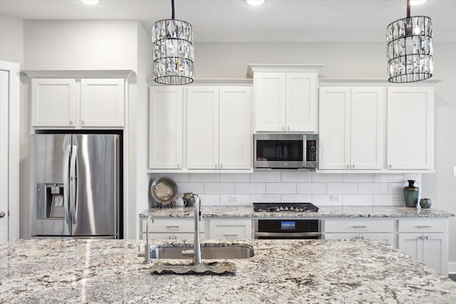 kitchen with appliances with stainless steel finishes, pendant lighting, tasteful backsplash, white cabinetry, and sink