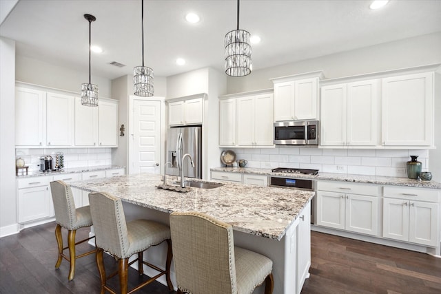 kitchen featuring a kitchen island with sink, decorative light fixtures, white cabinets, and appliances with stainless steel finishes