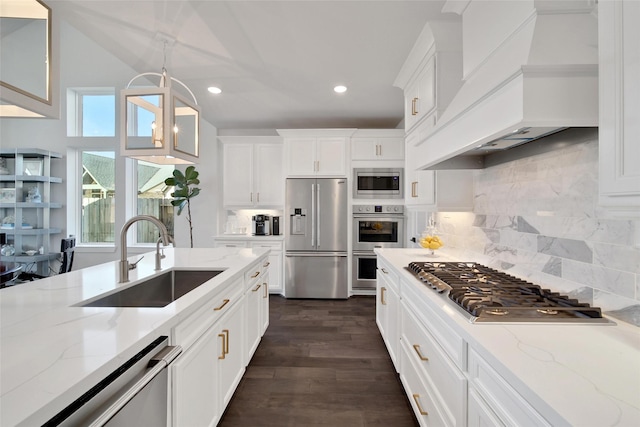 kitchen featuring light stone counters, a sink, appliances with stainless steel finishes, custom exhaust hood, and pendant lighting