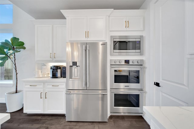 kitchen with dark wood-style floors, appliances with stainless steel finishes, light stone countertops, white cabinetry, and backsplash