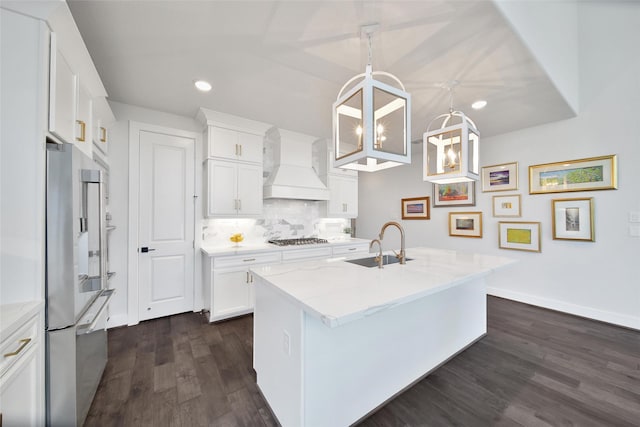 kitchen with white cabinets, custom range hood, hanging light fixtures, and a sink