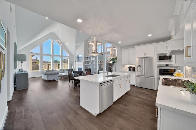 kitchen featuring appliances with stainless steel finishes, open floor plan, light stone countertops, a kitchen island with sink, and pendant lighting