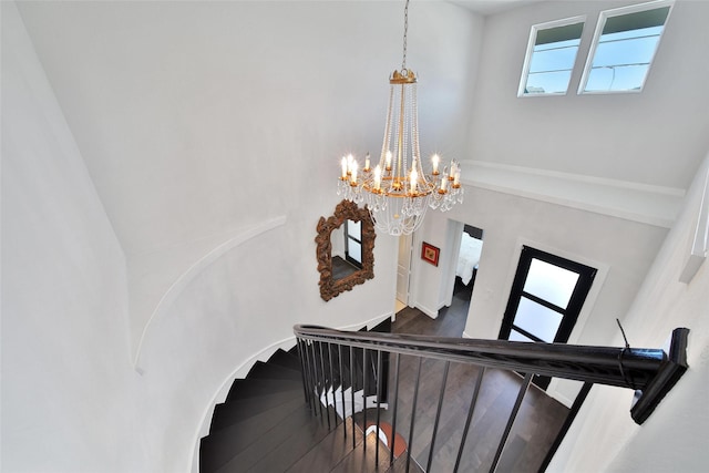 staircase with a notable chandelier, a towering ceiling, and wood finished floors