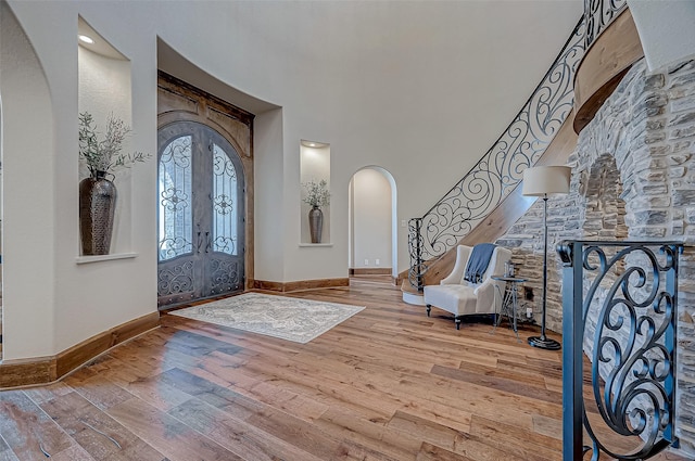 entrance foyer with arched walkways, hardwood / wood-style flooring, a towering ceiling, baseboards, and french doors