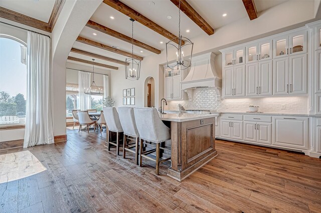 kitchen featuring arched walkways, light wood finished floors, light countertops, tasteful backsplash, and custom range hood