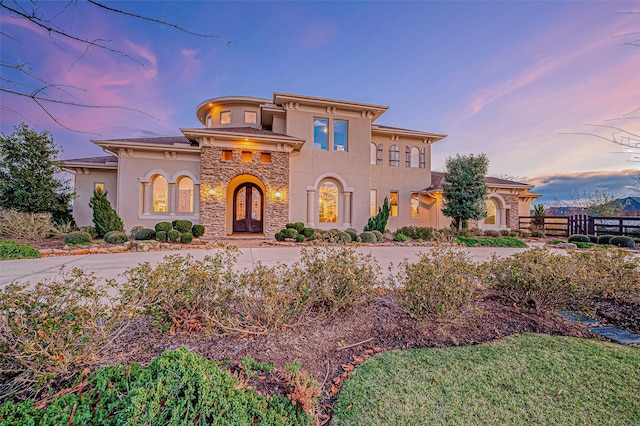 mediterranean / spanish home featuring stone siding, fence, and stucco siding