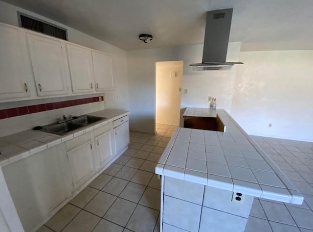 kitchen with light tile patterned flooring, sink, white cabinetry, island range hood, and tile counters