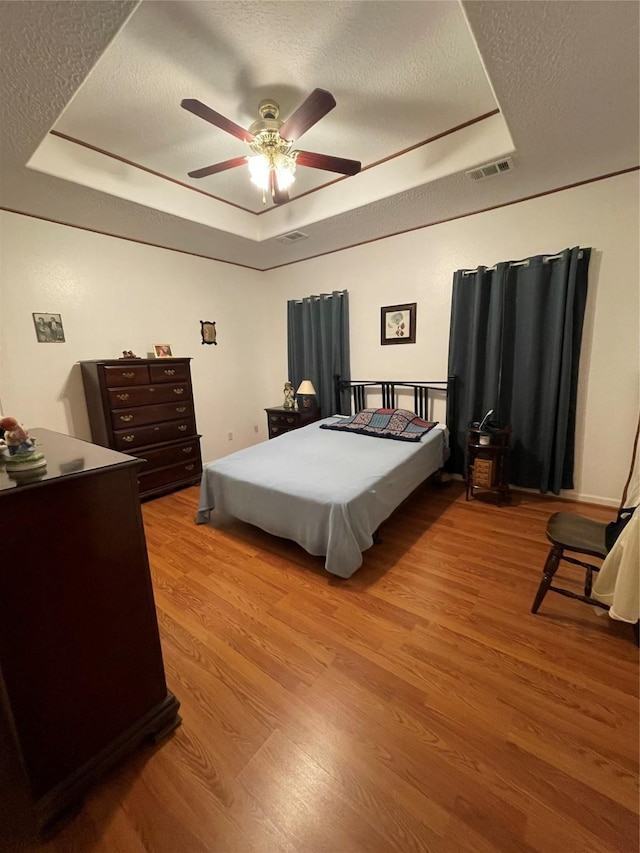 bedroom featuring light wood-type flooring, a raised ceiling, visible vents, and a textured ceiling