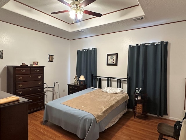 bedroom featuring wood finished floors, a raised ceiling, visible vents, and a ceiling fan