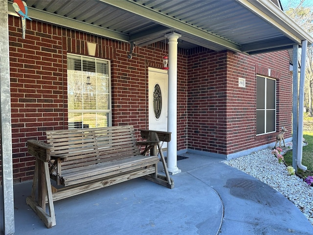 doorway to property featuring a porch and brick siding