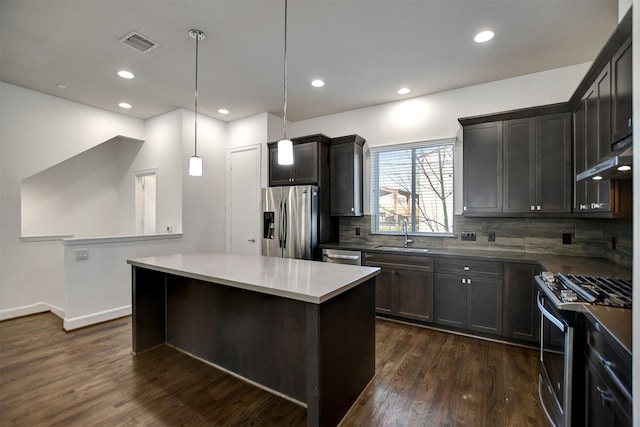 kitchen featuring appliances with stainless steel finishes, dark hardwood / wood-style floors, decorative light fixtures, sink, and a center island