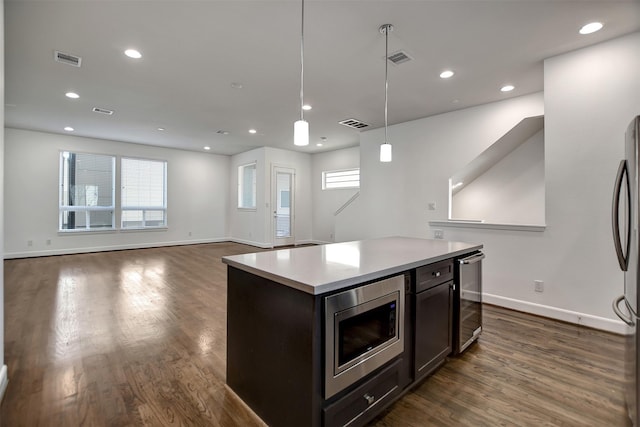 kitchen featuring hanging light fixtures, appliances with stainless steel finishes, dark hardwood / wood-style floors, a kitchen island, and beverage cooler