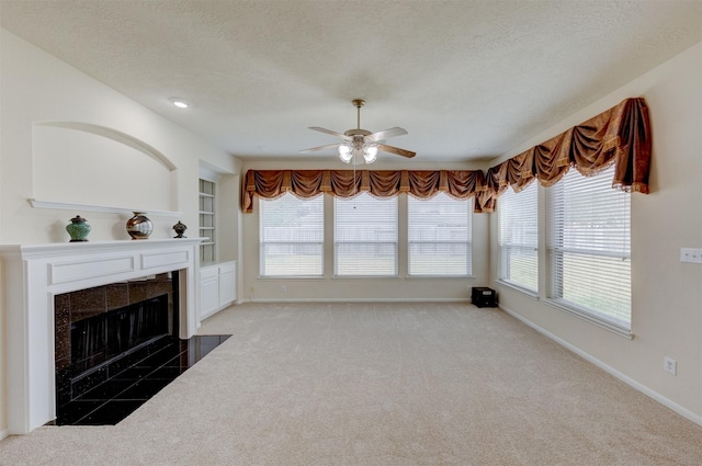 living room with built in shelves, a textured ceiling, ceiling fan, a tiled fireplace, and carpet