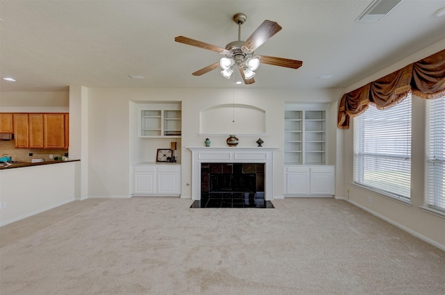 unfurnished living room with a tiled fireplace, light carpet, built in features, and ceiling fan