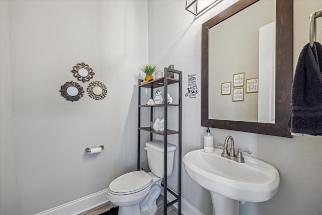 half bath featuring toilet, baseboards, and a sink